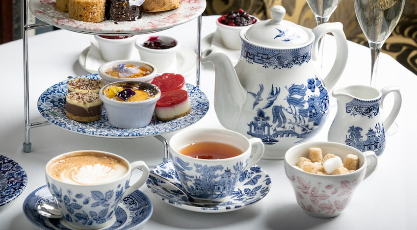 a table full of teatime accessories: a teapot, teacups, finger sandwiches and sweets