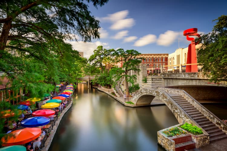 san antonio's river walk, complete with a stone bridge and colorful umbrellas