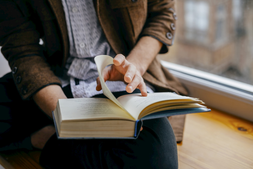 A person reading a book near a window.