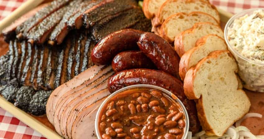 a plate filled with beans, sausages, brisket, and other texas bbq