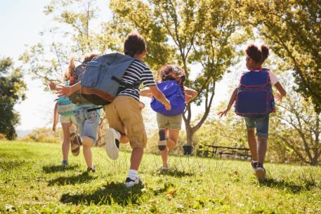 a group of children with backpacks run in a park