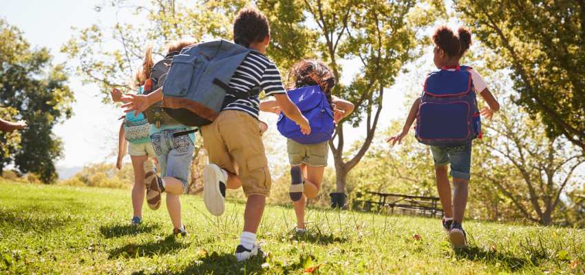 a group of children with backpacks run in a park