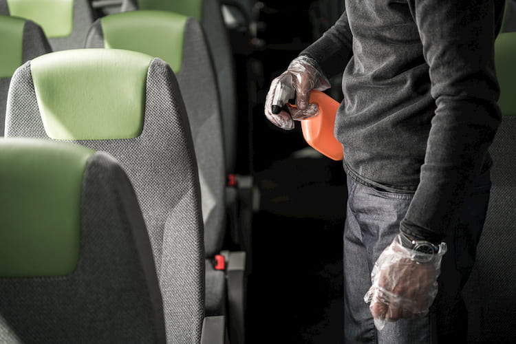 a man spraying disinfectant on a bus armrest