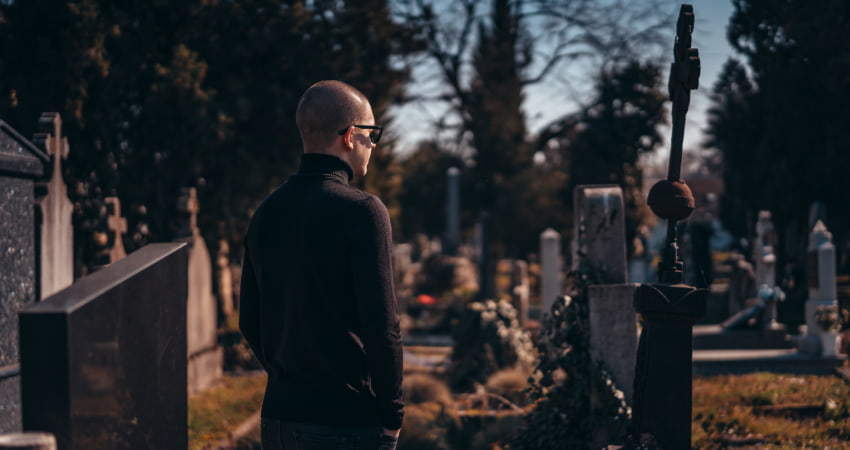 A lone man in black stands in an old cemetery