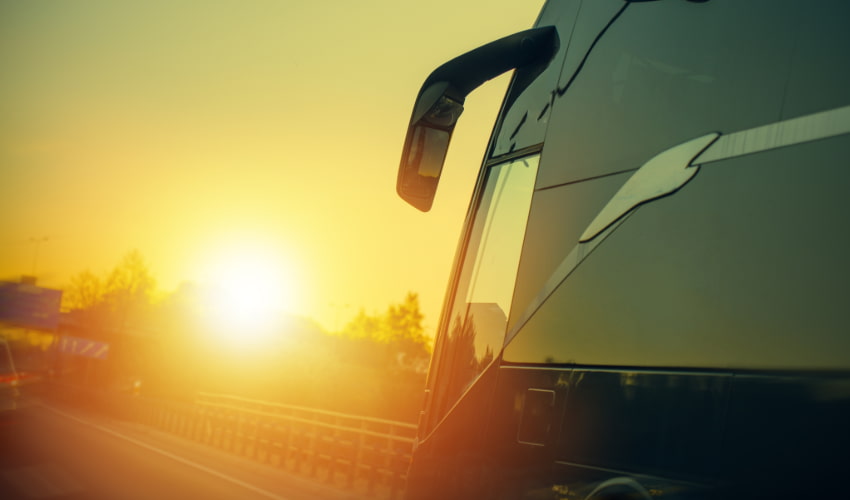 A charter bus drives on an empty highway, towards the sunset