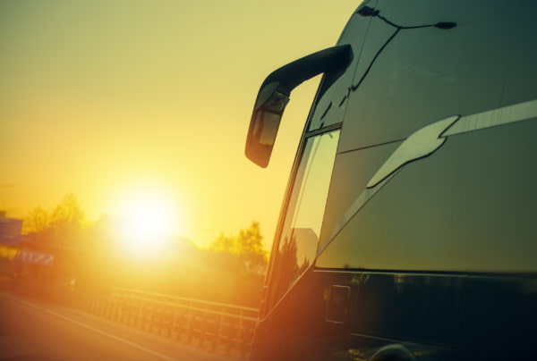 A charter bus drives on an empty highway, towards the sunset