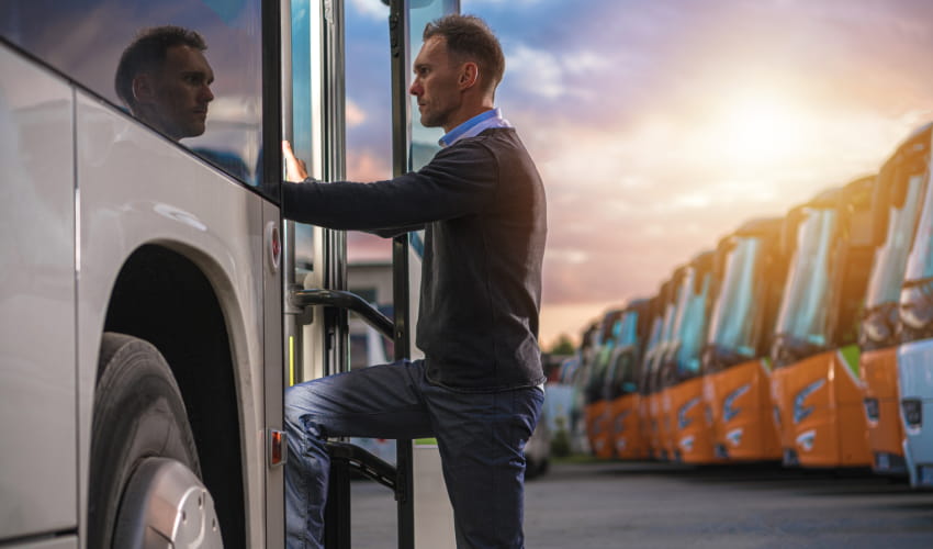 A man enters a charter bus entrance, with a sunset and a row of orange charter buses visible in the background