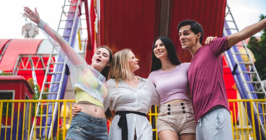 A group of four teens embrace and smile in an amusement park