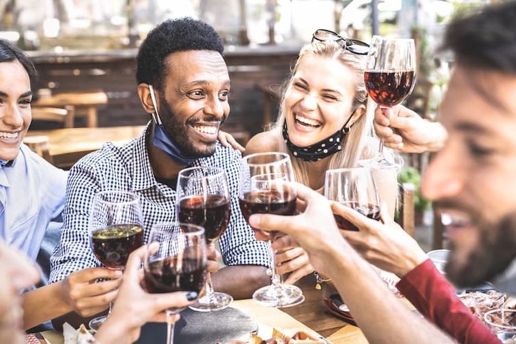 People clinking glasses of wine outside with masks lowered