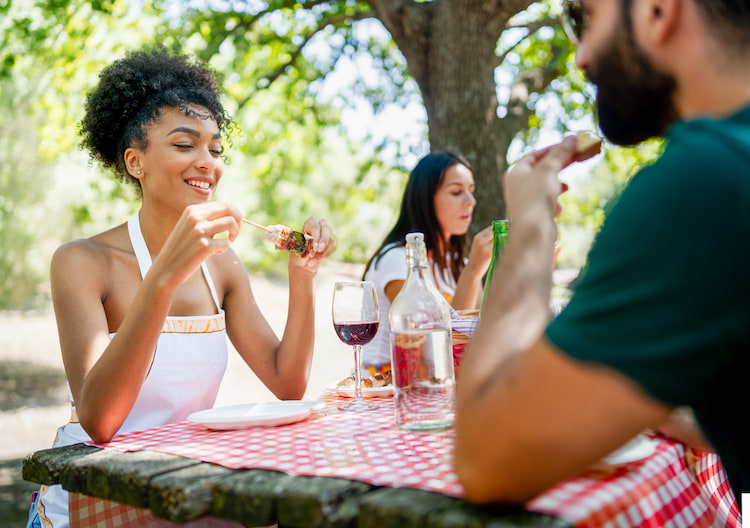 friends smile while they eat around an outdoor table