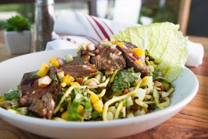 a bed of greens with a thinly-sliced steak on top