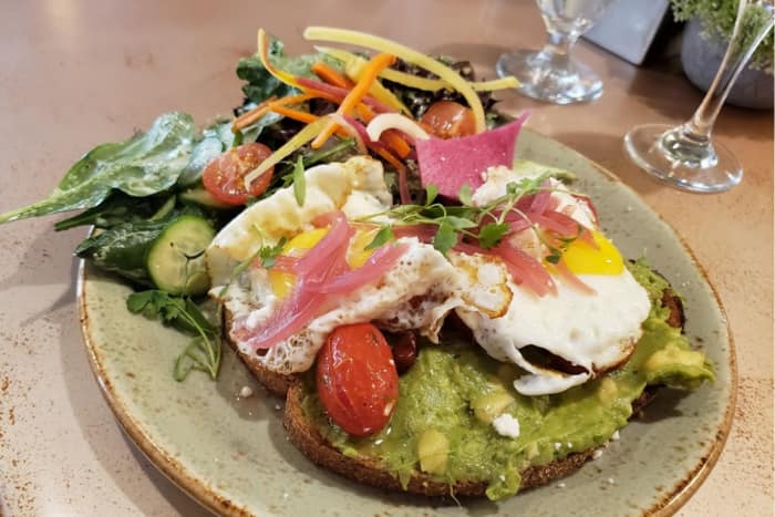 avocado toast topped with an egg, pickled red onions, and greens