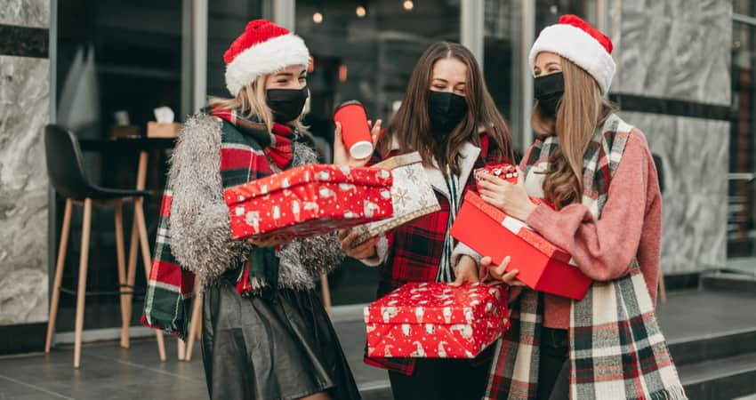 A group of friends in holiday attire and masks holding gifts