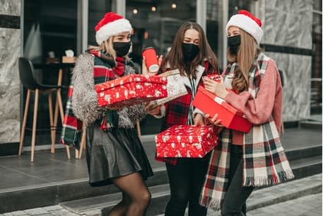 A group of friends in holiday attire and masks holding gifts