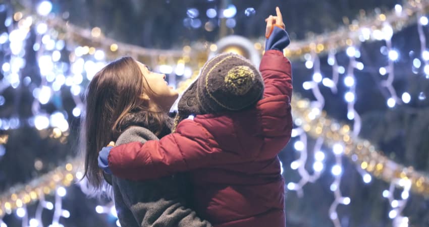 A child being held by an adult while looking up at holiday lights