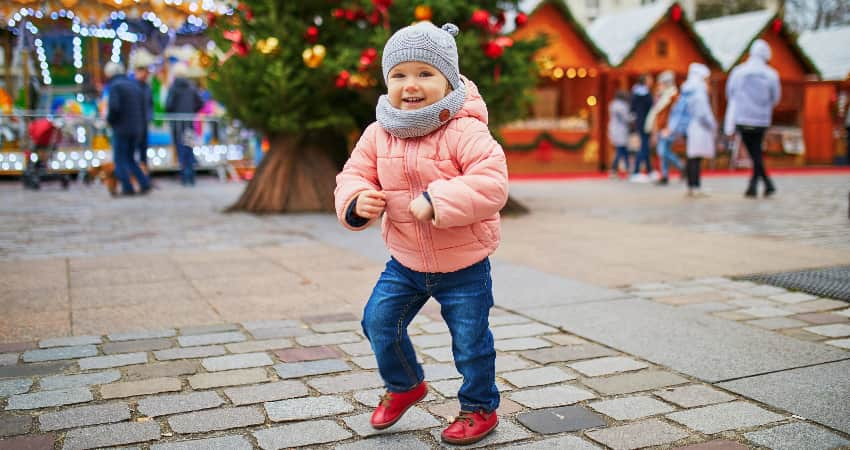 A small child in a hat and thick coat smiles and plays in a holiday street festival