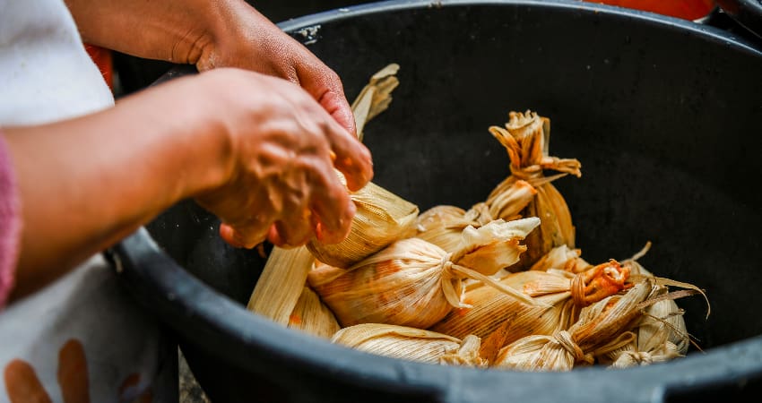 A woman places hand-made tamales in a bowl