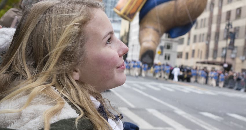 A teen girl watches a large balloon fly by in a city parade