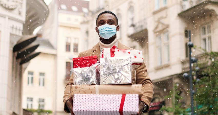 A man wearing a face mask holds an armful of holiday gifts