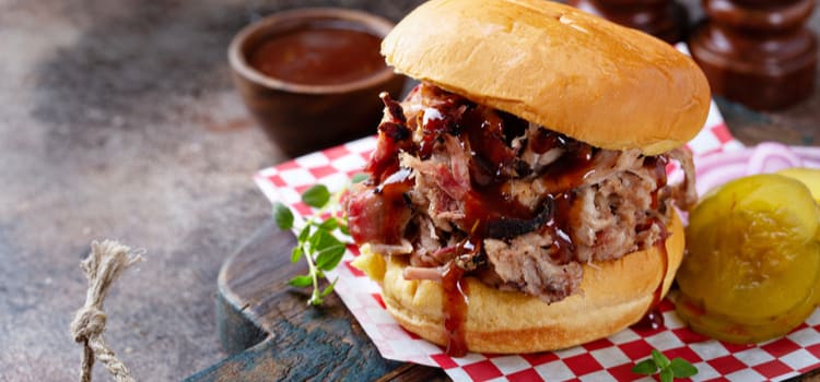 a close-up of a pulled pork bbq sandwich with sauce dripping over the meat