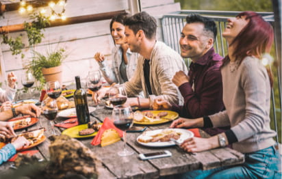 friends sit around a table and laugh while enjoying a barbecue meal