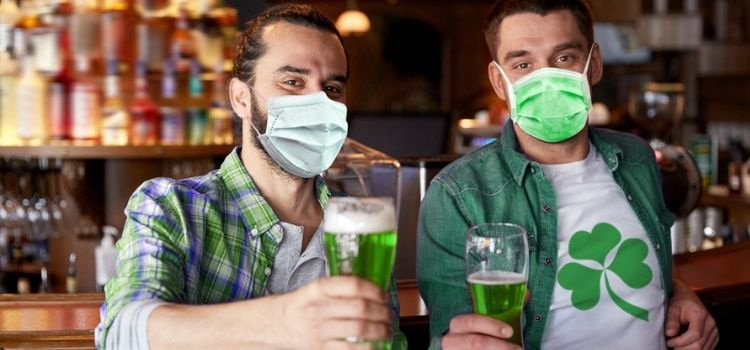 happy male friends wearing face protective medical mask for protection from virus disease drinking green beer at bar