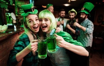 Two girls in a wig and a cap in a bar celebrate St. Patrick's Day.