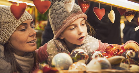 An adult and child admire Christmas ornaments at an outdoor market