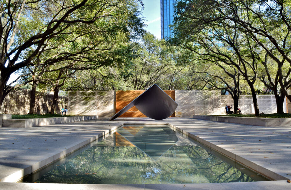 an angular art piece outside of a Dallas museum, with a reflecting pond beneath it
